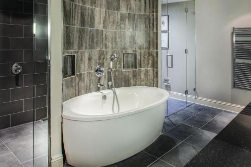 a white bath tub in a bathroom with tiles at De Vere Wokefield Estate in Reading