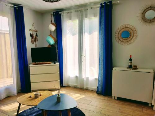 a living room with blue curtains and a table and a tv at La Cabane de Didi in Andernos-les-Bains