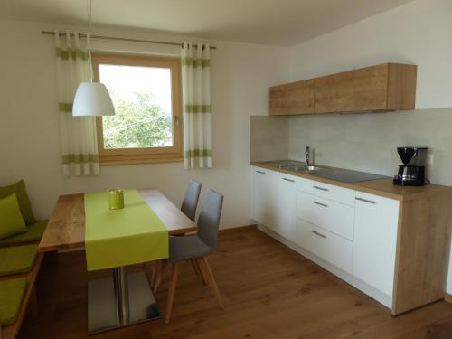 eine Küche mit einem Holztisch, einem grünen Tisch und Stühlen in der Unterkunft Ferienwohnungen Ederhof in Schenna