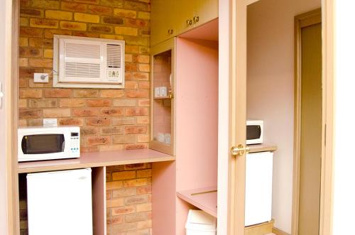 a kitchen with a microwave and a brick wall at Pines Country Club Motor Inn in Shepparton