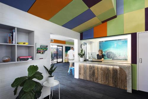 un hall de bureau coloré avec une femme assise dans un bar dans l'établissement Spinners Hostel, à Perth