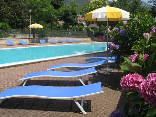 three lounge chairs and an umbrella next to a swimming pool at Hotel La Pineta in Cogoleto