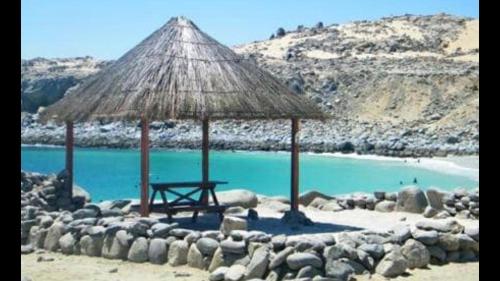 a beach with a straw umbrella and blue water at Condominio Bahia Inglesa in Bahia Inglesa