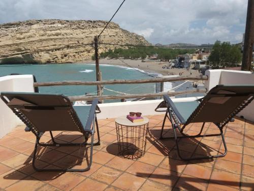 2 Stühle und ein Tisch auf einem Balkon mit Strand in der Unterkunft Absolute Matala in Matala