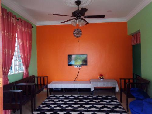 a room with an orange wall with a table and a ceiling fan at Masam2maniss Homestay in Melaka
