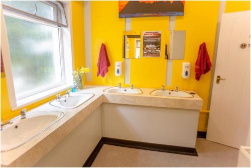 a yellow bathroom with two sinks and a window at Loch Ness Lochside Hostel, Over 16s Only in Invermoriston