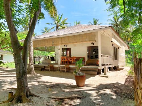 a small white house with a porch with a tree at Vayam Boutique Resort Gili Asahan in Gili Asahan