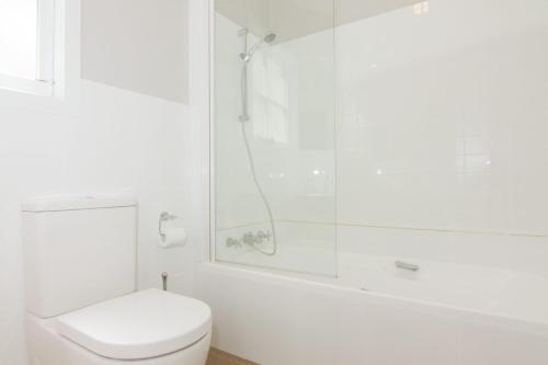 a white bathroom with a shower and a toilet at Atticus Cottage in Bright