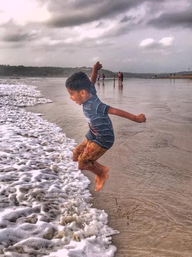 a young boy jumping into the water on the beach at Primavera Holiday Homes-FAMILY RUN GOAN GUEST HOUSE in Candolim