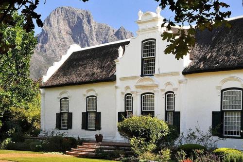 una casa blanca con una montaña en el fondo en GORDON's SHORE LUXURY APARTMENTS - Solar Powered en Gordonʼs Bay