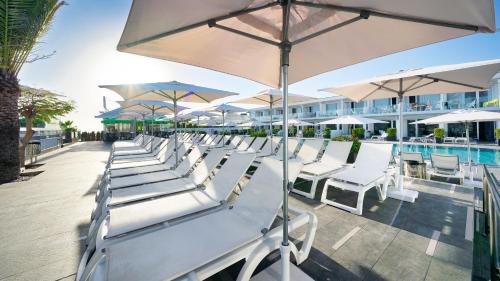 a row of white chairs and umbrellas next to a pool at Ura Lara Adults Only in Puerto Rico de Gran Canaria