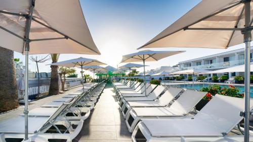 a row of white lounge chairs and umbrellas at a resort at Ura Lara Adults Only in Puerto Rico de Gran Canaria