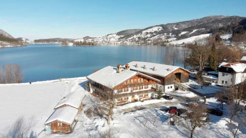 a large building in the snow next to a lake at Der Anderlbauer am See in Schliersee