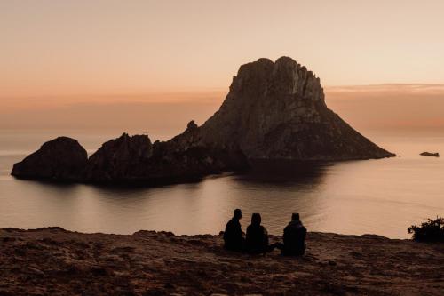 a group of three people sitting on a beach near the water at OKU Ibiza in San Antonio