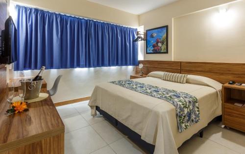 a bedroom with a bed and a table and blue curtains at Rede Andrade Riviera Premium in Salvador