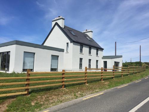 a white house with a fence next to a road at Farmhouse Boutique in Ballyheigue
