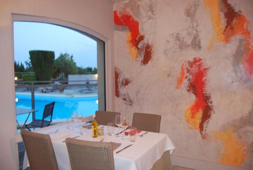 a dining room with a table and a painting on the wall at Logis Hôtel Restaurant Les Aubuns in Caissargues