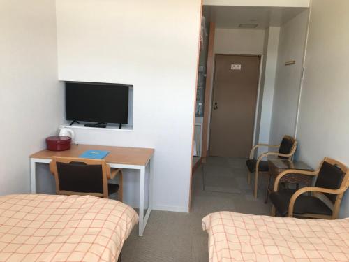 a room with a desk and a tv and two beds at Fujibou Hotel in Fujikawaguchiko