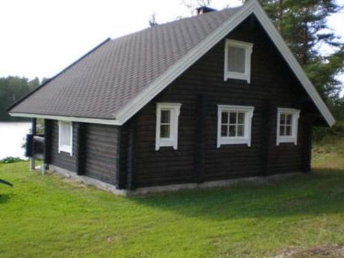 een klein zwart huis met witte ramen op een groen veld bij Holiday Home 6144 by Interhome in Jäniskylä