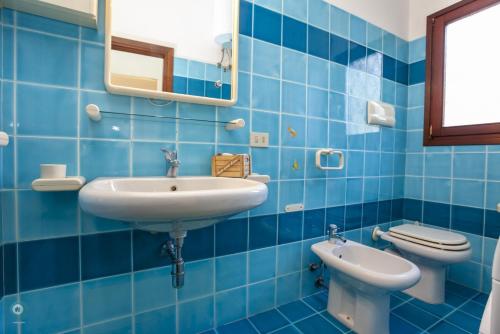 a blue tiled bathroom with a sink and a toilet at Villino Funtana Bilo in San Teodoro