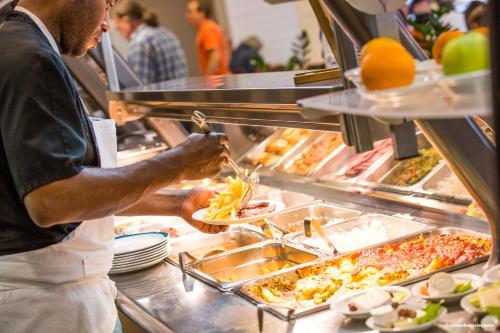 un homme prépare de la nourriture dans un buffet dans l'établissement Auberge de Jeunesse Youth Hostel Ethic étapes Saint Malo, à Saint-Malo