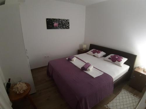 a bedroom with a bed with purple sheets and pillows at LANELU apartman in Rogoznica