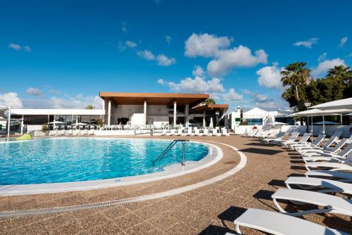 a swimming pool with white chairs and a pavilion at Hyde Park Lane Villas in Puerto del Carmen