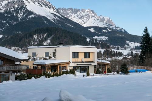 a house in the snow with mountains in the background at Appartement Hoschek in Scheffau am Wilden Kaiser