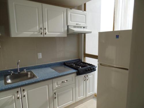 a kitchen with white cabinets and a sink and a refrigerator at Hotel Suites Bernini in Guadalajara