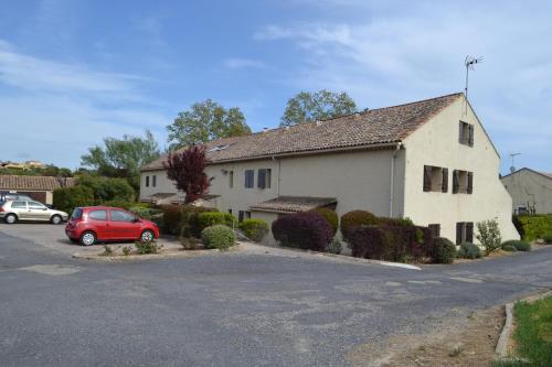 a white house with a red car parked in a parking lot at L'instant Canal in Capestang