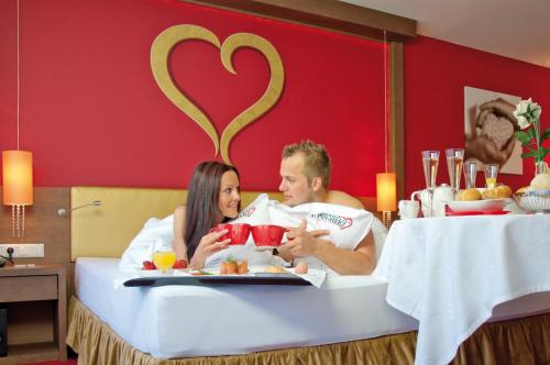 a man and woman sitting in a bed with a tray of food at Alpen-Herz Romantik & Spa - Adults Only in Ladis