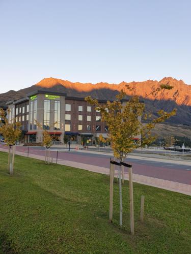 un bâtiment avec des arbres dans l'herbe en face d'une route dans l'établissement Wyndham Garden Queenstown, à Queenstown