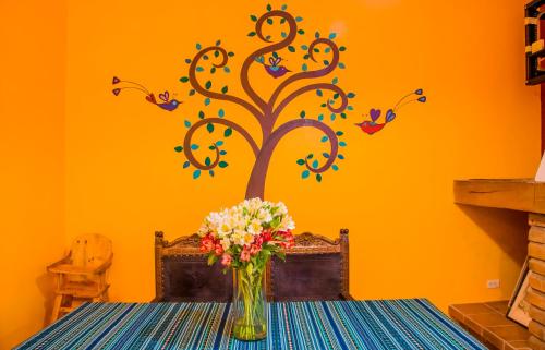 a table with a vase of flowers and a tree on a wall at Hostal Riviera Sucre in Otavalo