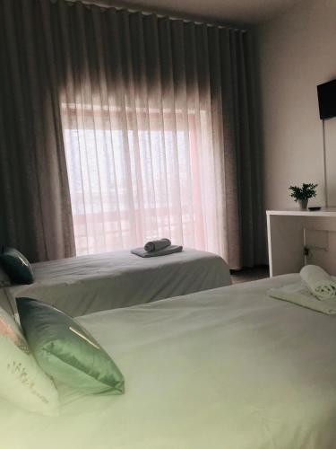 two beds in a hotel room with a window at Dom Quixote apartamentos turísticos in Praia de Mira