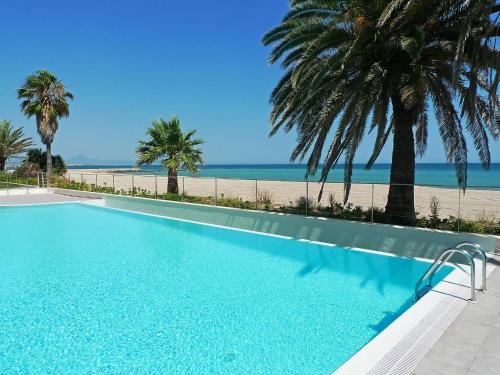 a swimming pool next to a beach with palm trees at Apartment Marenia by Interhome in Denia