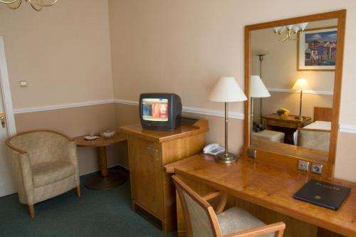 a room with a desk with a television and a mirror at Dr. Adler Spa & Kurhotel in Františkovy Lázně