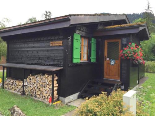 een klein zwart huis met een stapel brandhout bij Apartment Abnaki- Chalet by Interhome in Gstaad