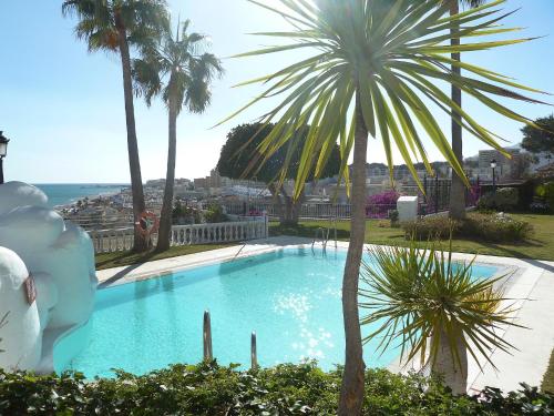 a swimming pool with a palm tree and the ocean at Apartment Castillo San Carlos in Torremolinos
