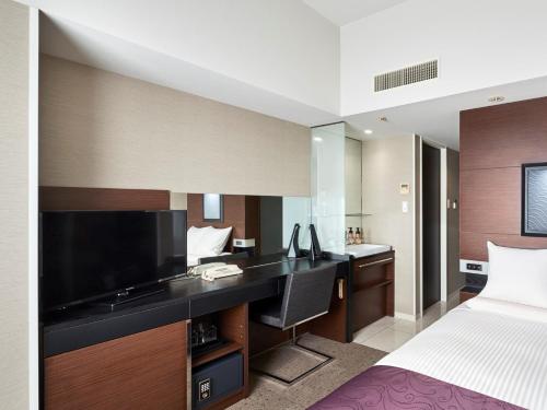 a bedroom with a bed and a desk with a television at HOTEL MYSTAYS Shimizu in Shizuoka