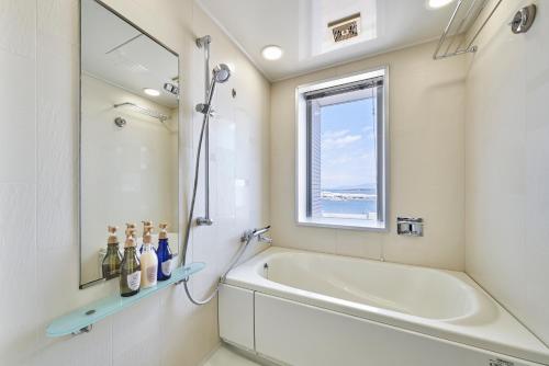 La salle de bains blanche est pourvue d'une baignoire et d'une fenêtre. dans l'établissement HOTEL MYSTAYS Shimizu, à Shizuoka