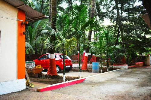 a red car parked in a parking lot with palm trees at Ashish Baug Cottage in Alibaug