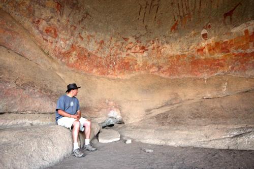 a man sitting in front of a rock wall at Big Cave Camp in Matopos