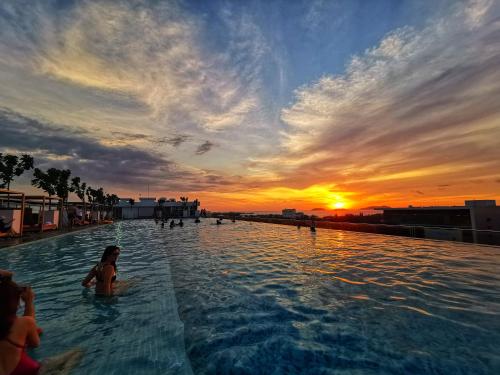 a woman in a infinity pool with a sunset in the background at JC Suites @ Sutera Avenue in Kota Kinabalu