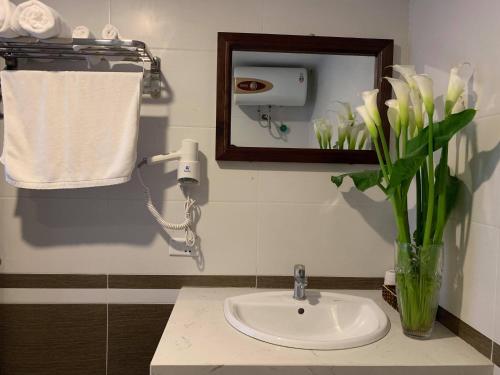 a bathroom sink with a mirror and a vase of flowers at Sapa Meriton Boutique Hotel in Sapa