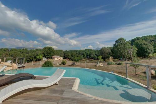 a large swimming pool with a wooden deck next to a field at Les Hauts de Cavanello in Zonza