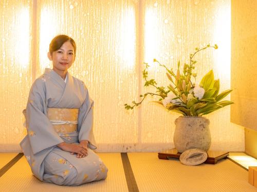 a woman sitting on the floor next to a vase at Nagominoyado Hanagokoro - Reopening in Mar 2024 in Hakone