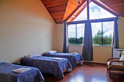 Cette chambre comprend deux lits et une grande fenêtre. dans l'établissement Pousada AlpenRose, à Campos do Jordão