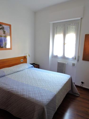 a bedroom with a bed with a white bedspread and two windows at Hotel Capri in Lesa