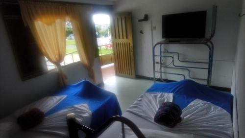 two beds with blue sheets in a room with a tv at Hospedaje El Viajero De Versalles in Calarcá