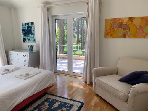 ein Schlafzimmer mit einem Bett und einem Stuhl sowie einer Glasschiebetür in der Unterkunft Aroeira Villa near Lisbon- Daydream PT in Charneca